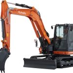 Photo of a Kubota KX085-5 brand 9 tonne excavator. The excavator is the standard Kubota orange and black and features a cab for the driver, bucket and treads.