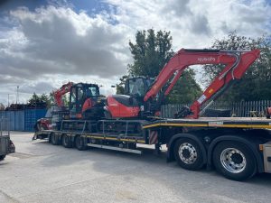 A photo of two red and black Kubota excavators being delivered to the Didcot Plant yard on the back of a very large trailer.