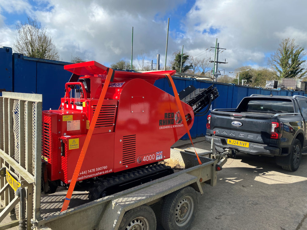 The bright red Rhino 4000 Mini Crusher tied on to a trailer and being towed to a site by a truck.