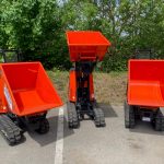 A photo of three new Kubota Tracked Dumpers. These bright red with black tracks dumpers are arranged in a row with their buckets at different heights.