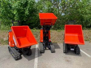 A photo of three new Kubota Tracked Dumpers. These bright red with black tracks dumpers are arranged in a row with their buckets at different heights.