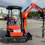 A photo of a bright orange and black mini excavator fitted with an earth auger in the Didcot Plant yard.